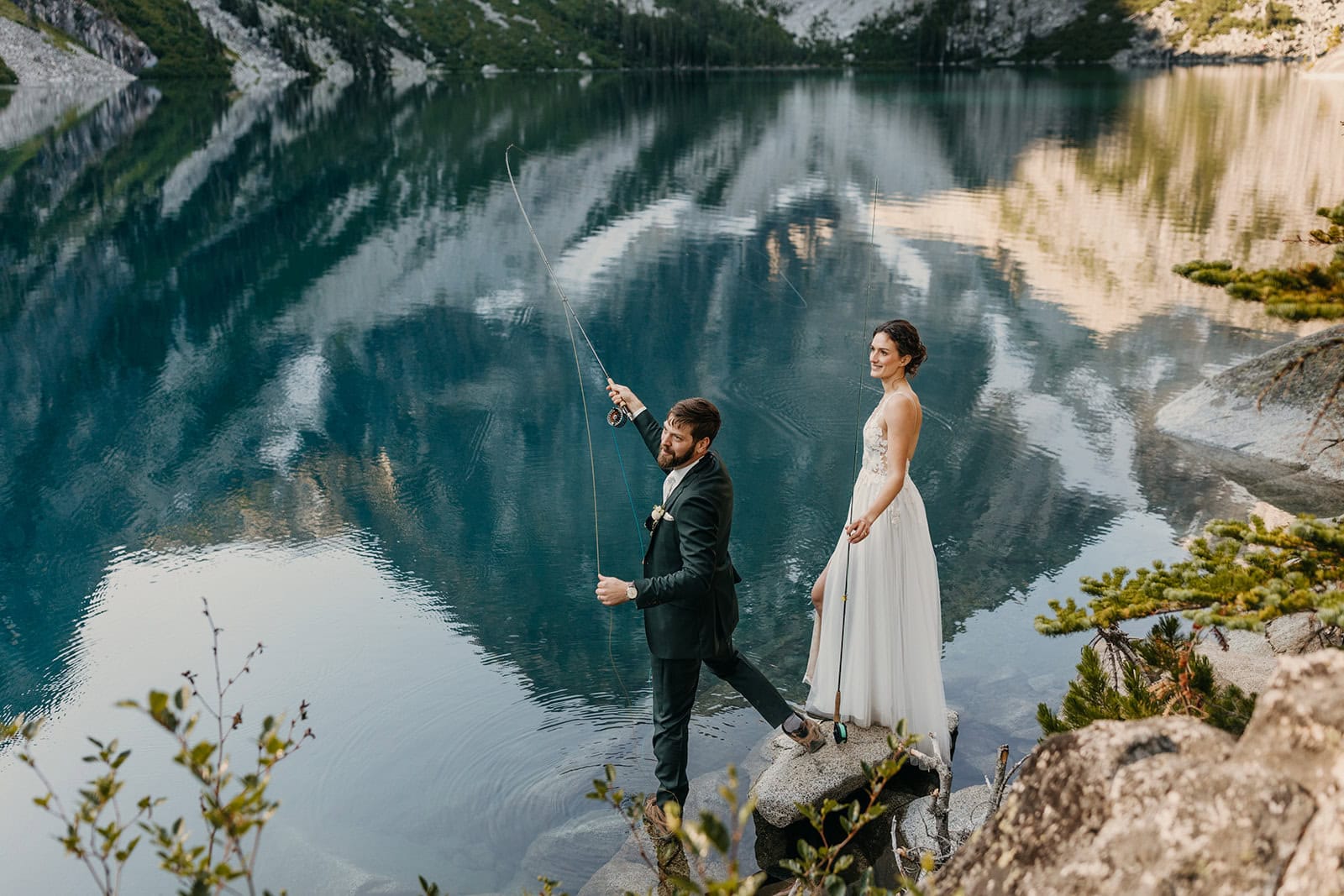 A couple fly fishes in their wedding attire on the edge of a lake in Leavenworth.