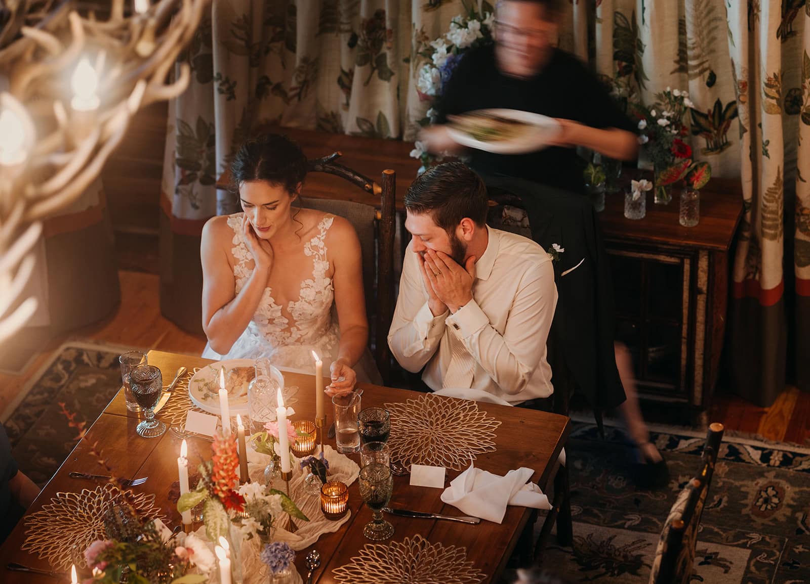 A bride and groom sit together while the chef brings their food to them.