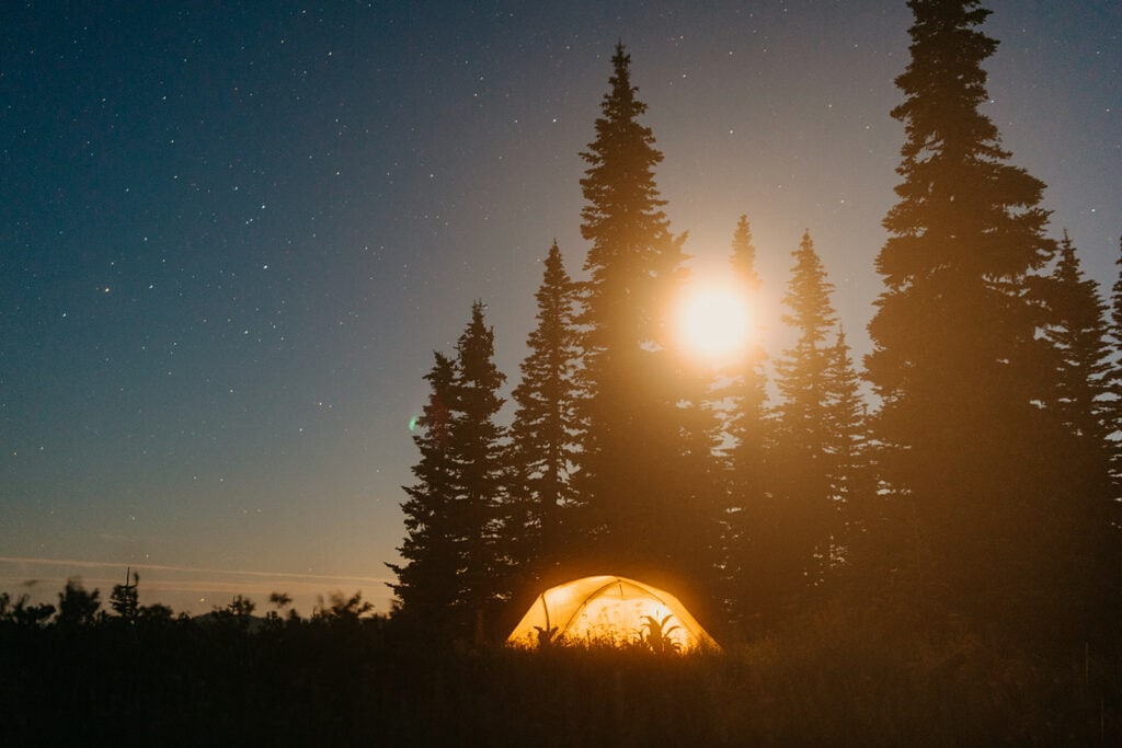 A tent under the stars while the moon comes up over the trees.
