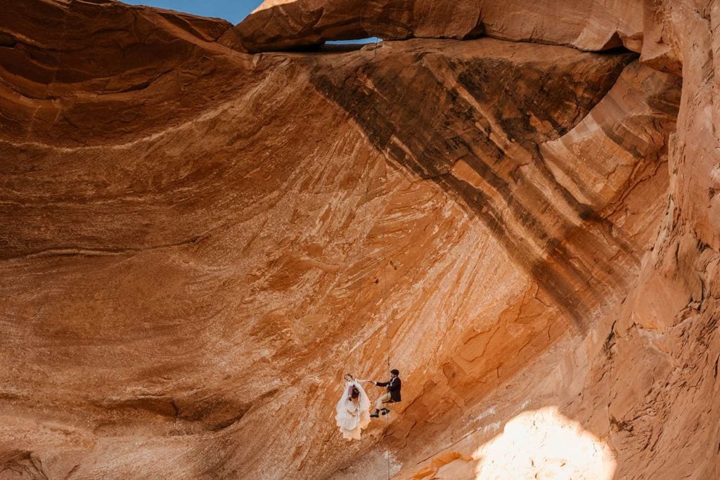 A bride and groom on a hanging rappel in Moab on a famous arch rock.