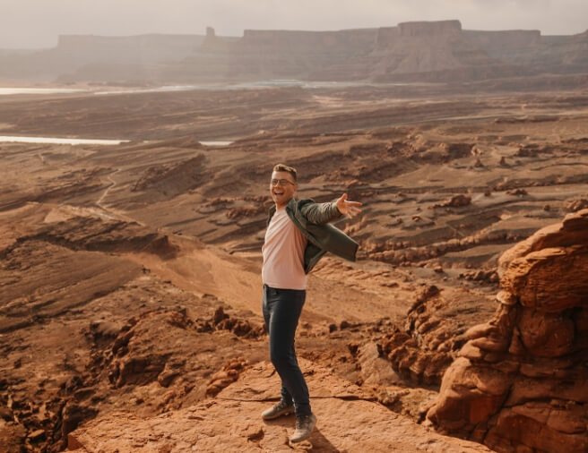 A person standing at the bottom of a canyon with their arms outstretched smiling