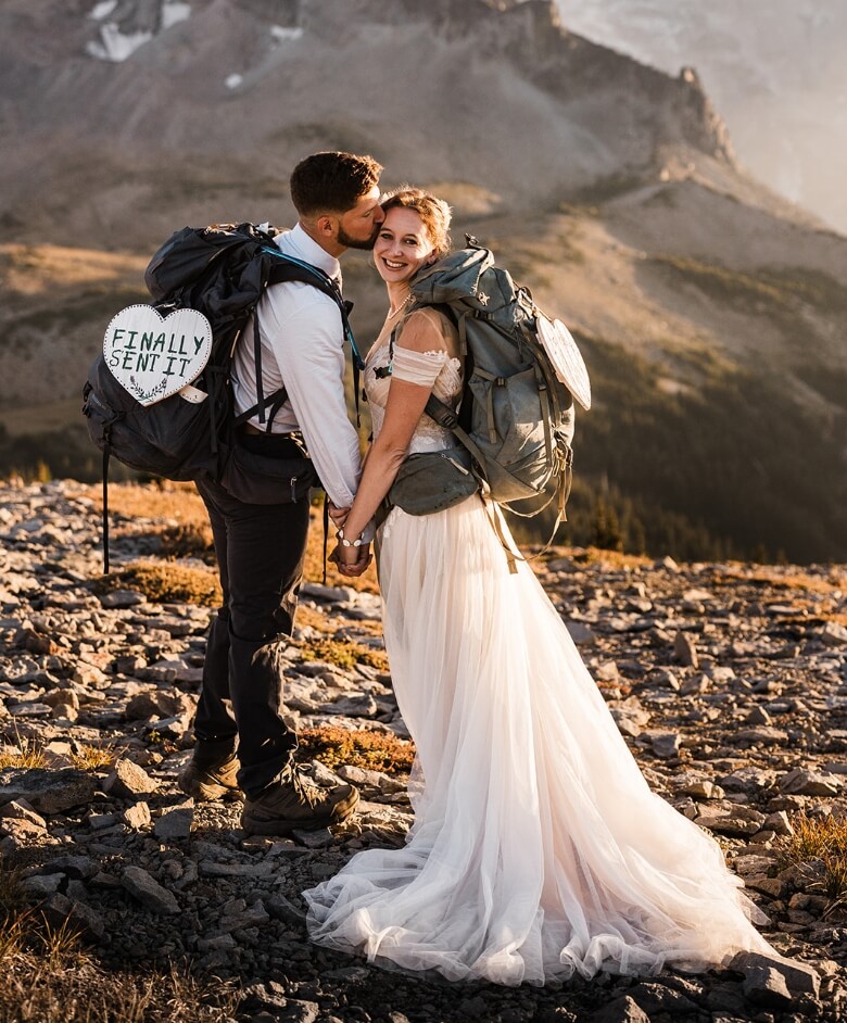 A person kissing their partner's cheek as they hold hands during their adventure elopement