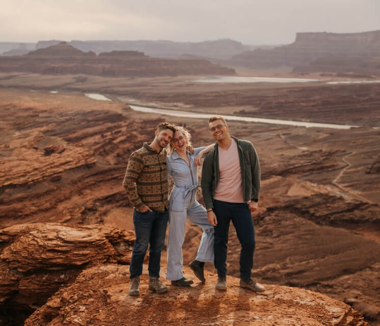 Three people smiling while standing on an overlook of a canyon