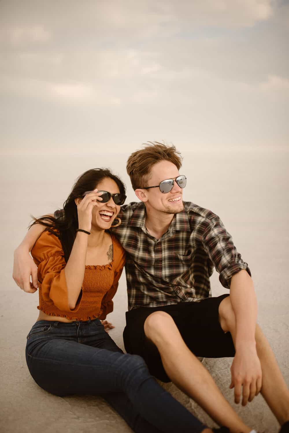 A man and woman smile together lookout at the sunset as the wind blows towards them.