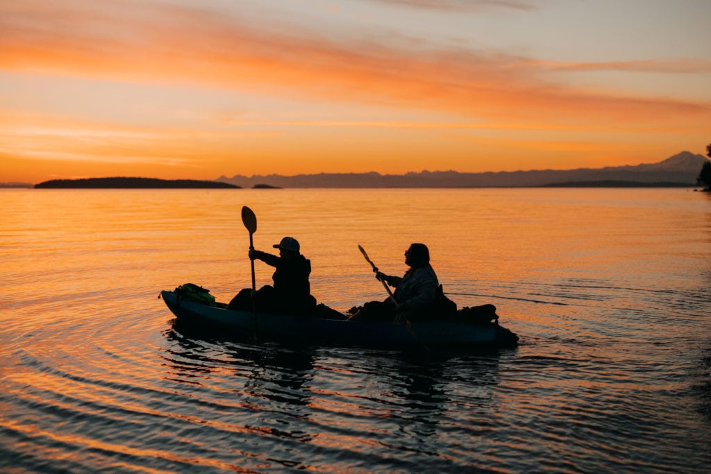A couple kayaking out to sea together during sunrise.