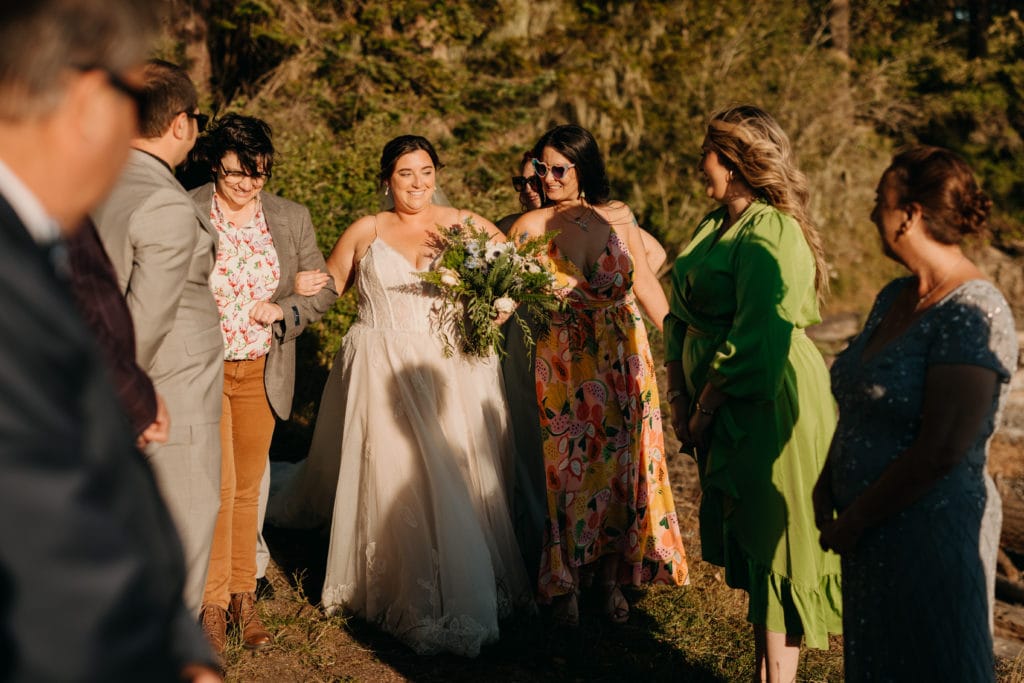 A bride walking down the aisle surrounded by her guests outside.