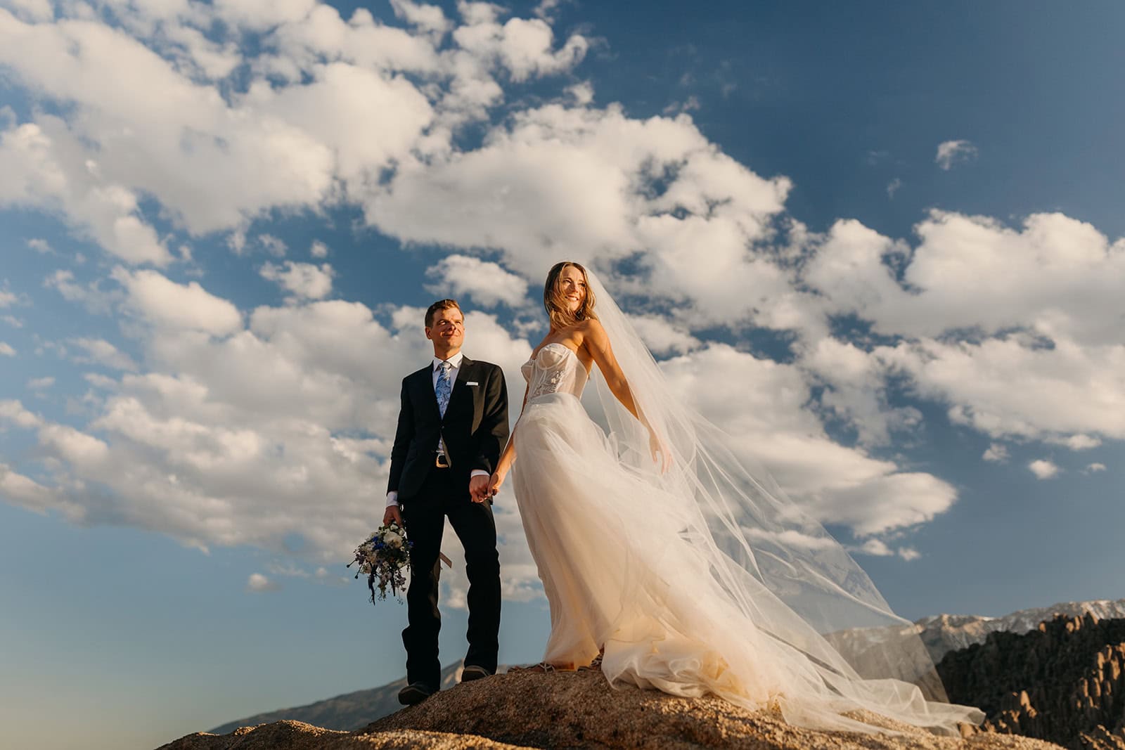 A bride show cases her elopement dress in the sunlight standing on top of a rock.