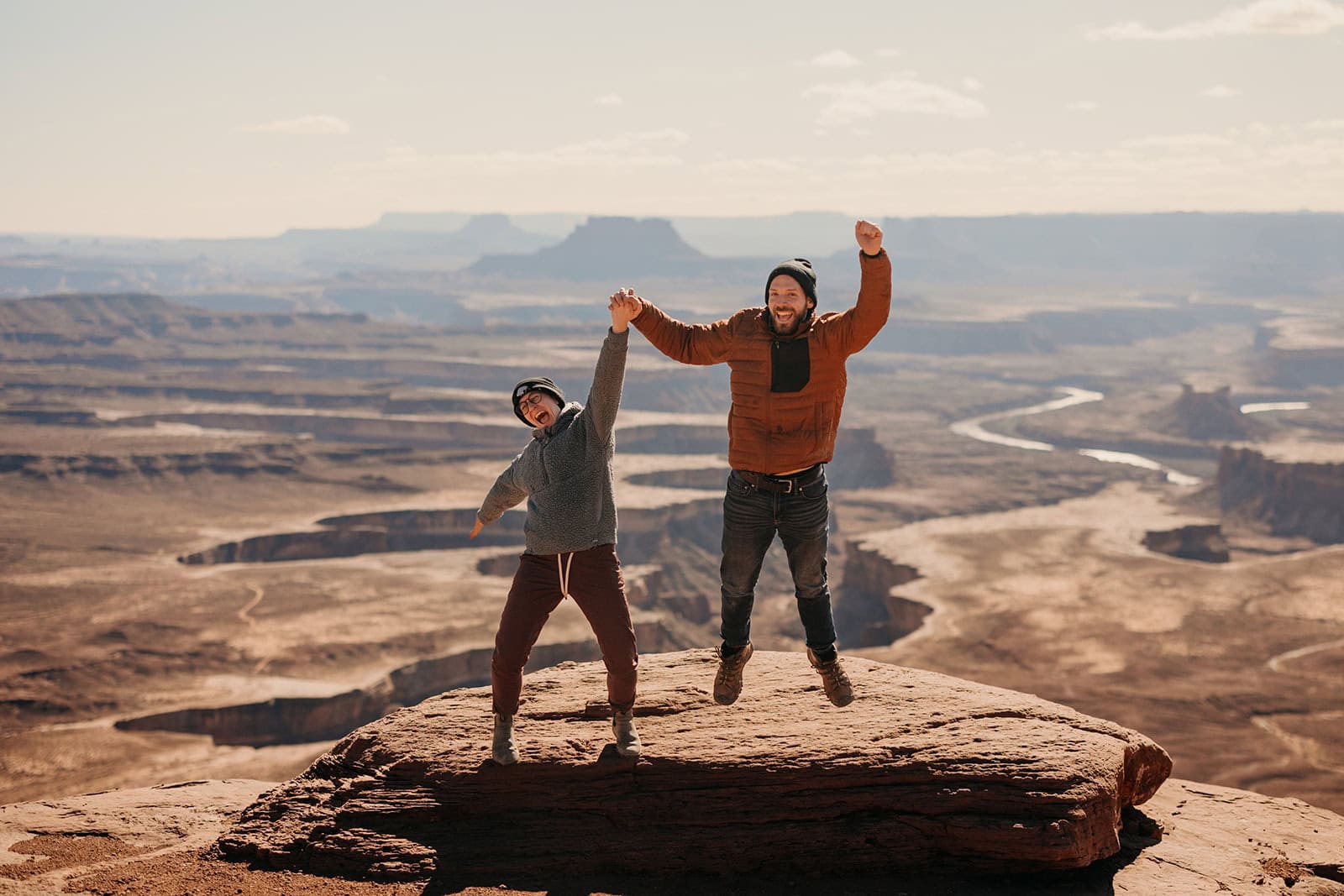 a couple holding hands and jumping with a view of Canyonlands national park in the background