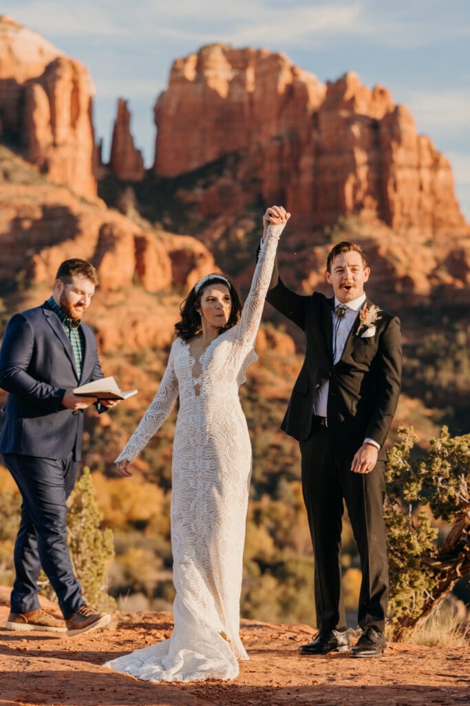 A bride and groom hold their hands up together in celebration of their first kiss