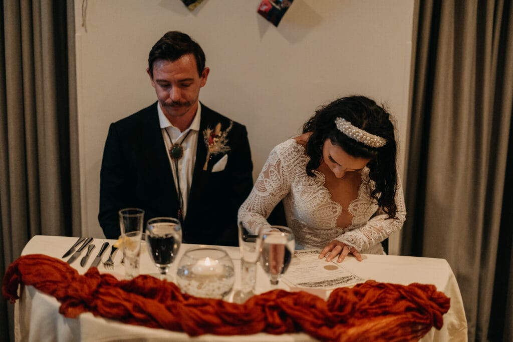 The bride and groom sit together and sign their marriage paperwork.