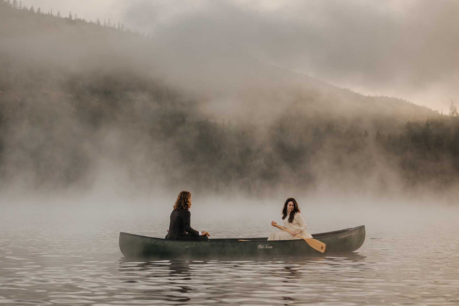 A couple canoes on a lake on a foggy morning to start off their wedding day.
