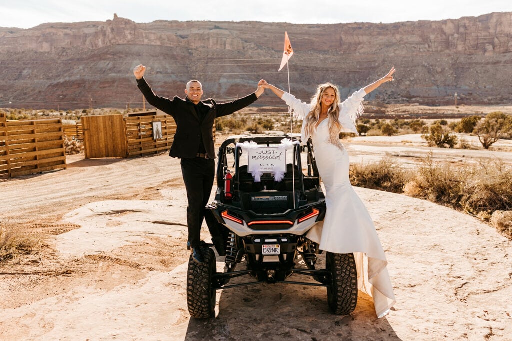 A couple stands on the top of an ATV together with a just married sign.