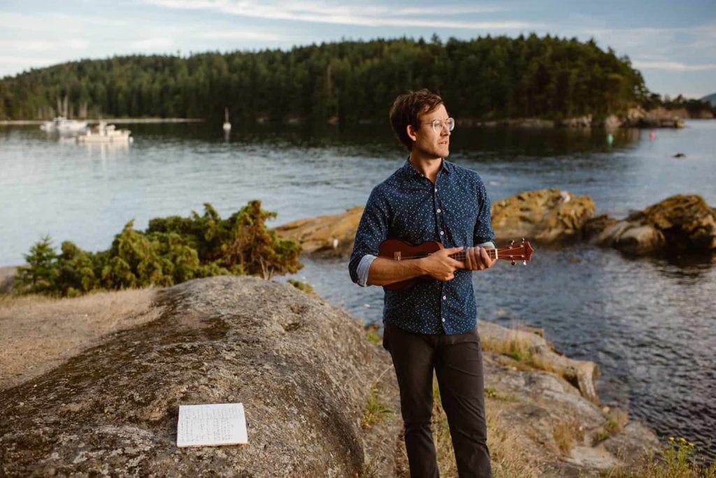 A guest of a wedding playing a ukulele while standing on the side of Sucia islands shore line.