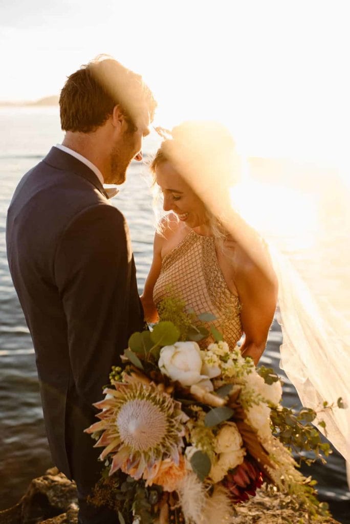 A detail picture of a bride and groom standing together while she holds a large and beautiful bouquet.