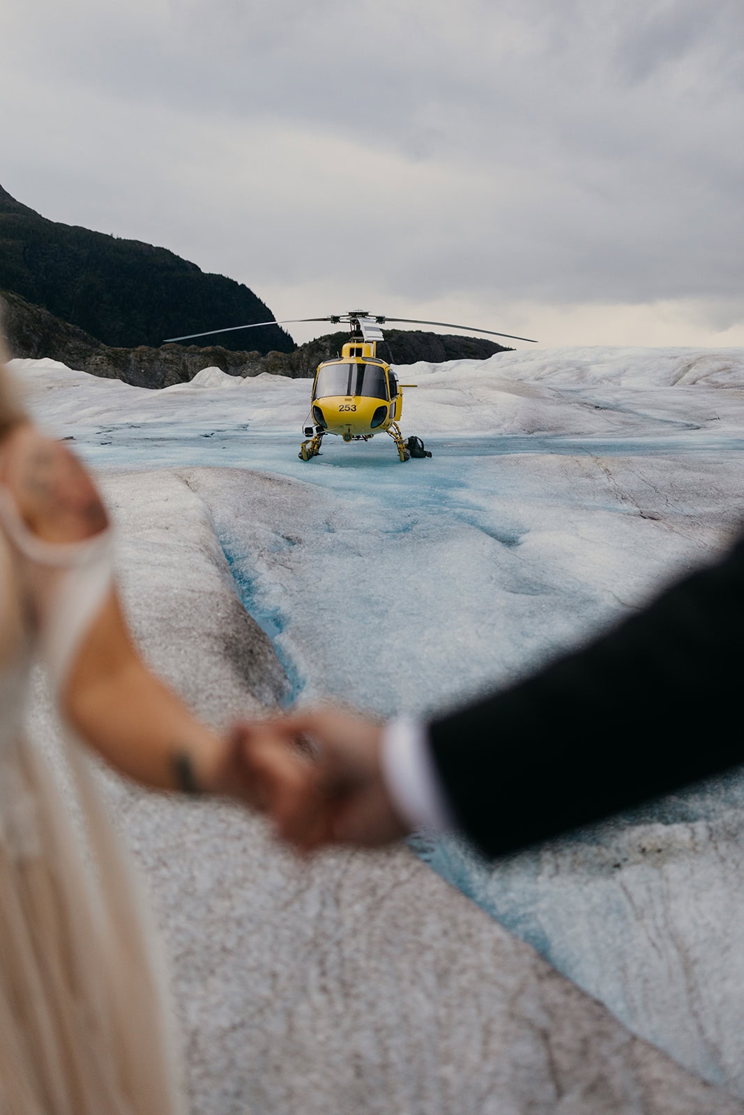 A photo of a helicopter on a glacier framed by a couple holding hands.