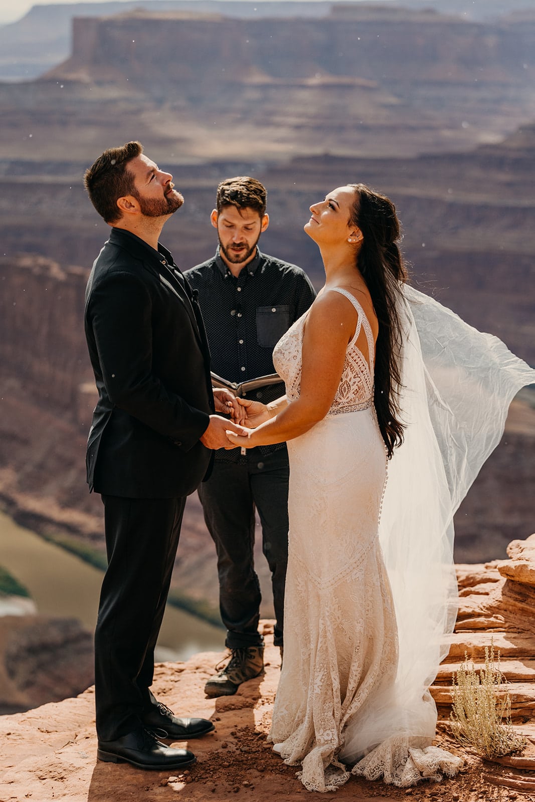 A couple holds hands and looks up at the rain on a sunny day as they elope.