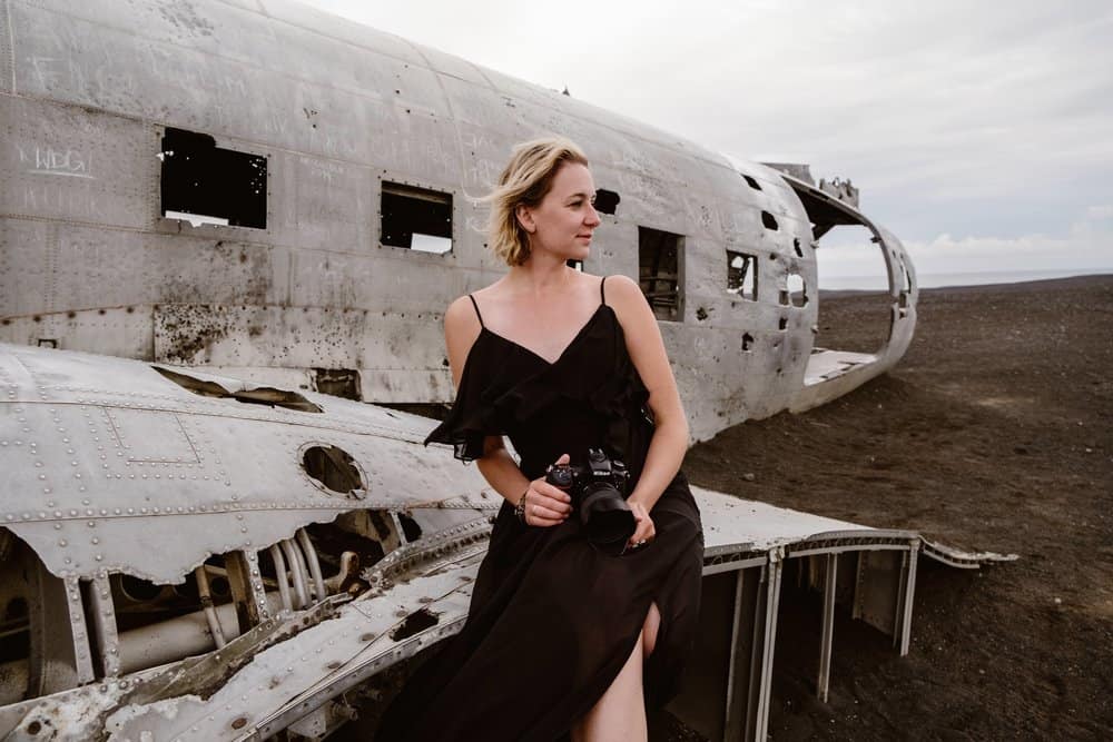Portrait of a girl in a black dress sitting on a crashed plane.