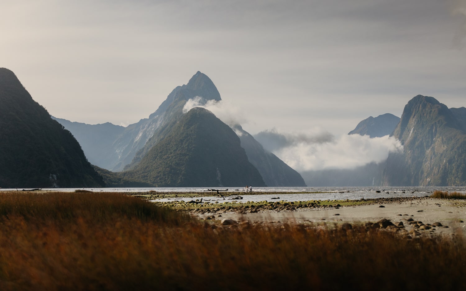 A couple walks out towards the water at Milford Sound.