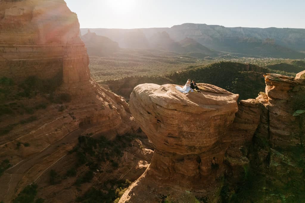 A bride and groom sit together at a vista during sunrise in Sedona.