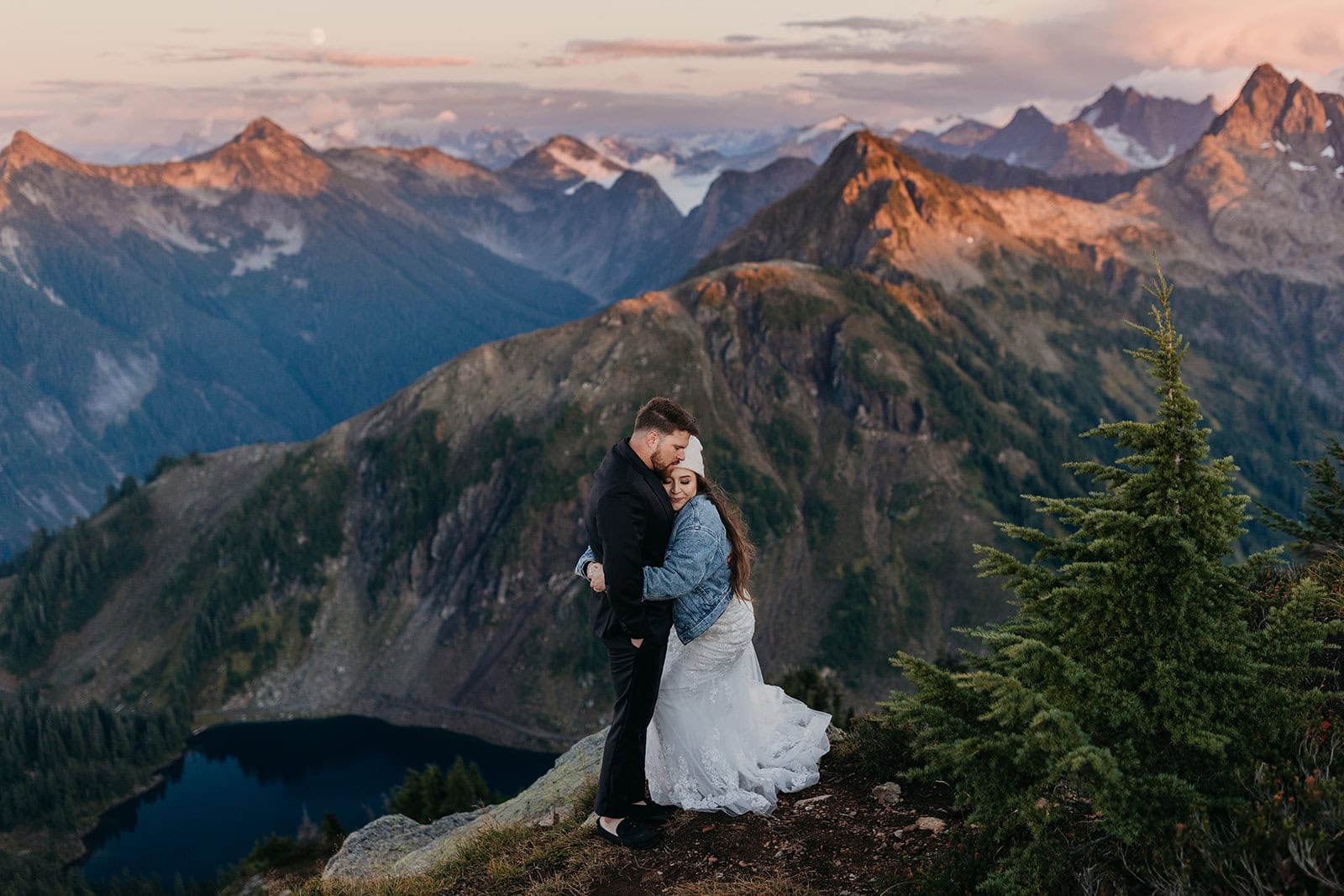 A couple shares an intimate hug as sunset casts beautiful colors over the mountain peaks.