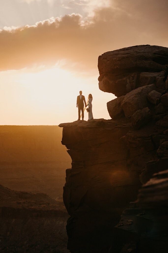A bride and groom stand together at Dead Horse Point at Sunset