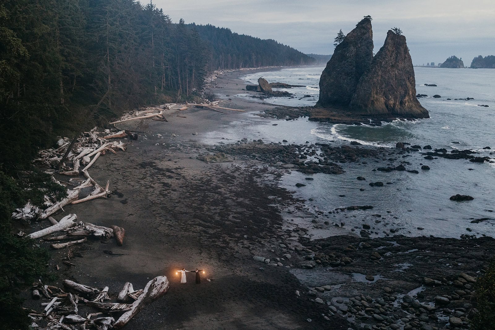 A couple holds lanterns as night falls on the coastline of Olympic national park.