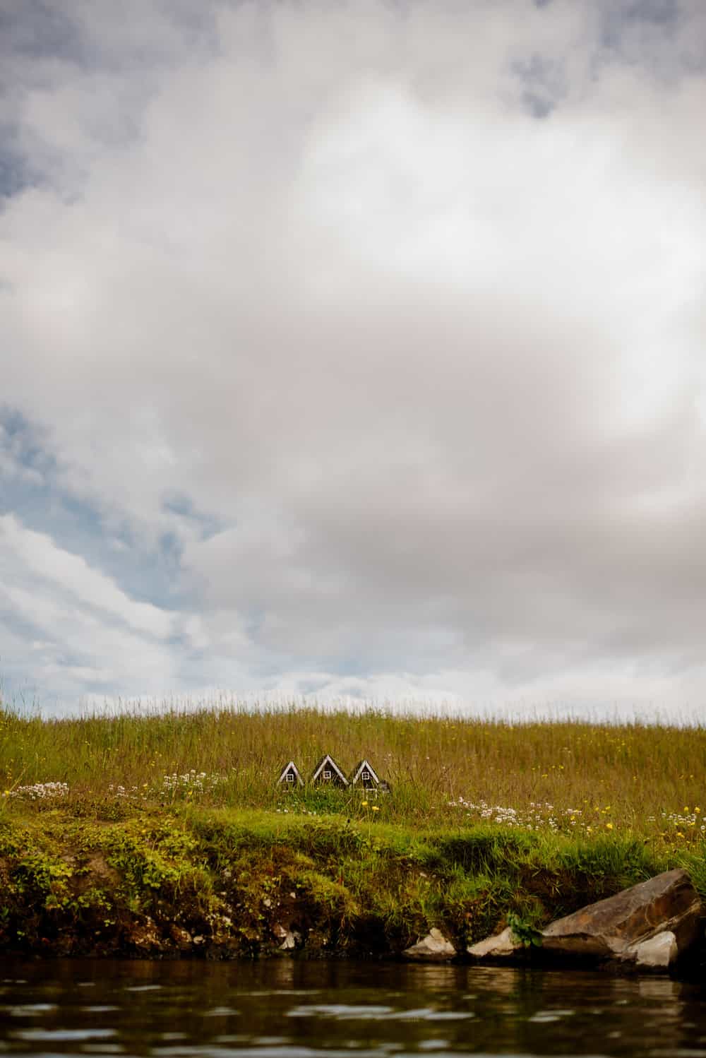 Landscape photo showcasing a fake small house by water and a lot of sky.