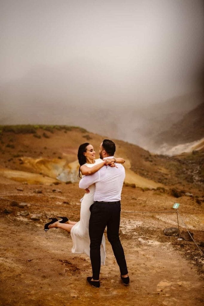 A bride looks at her groom lovingly as he holds her in Iceland.