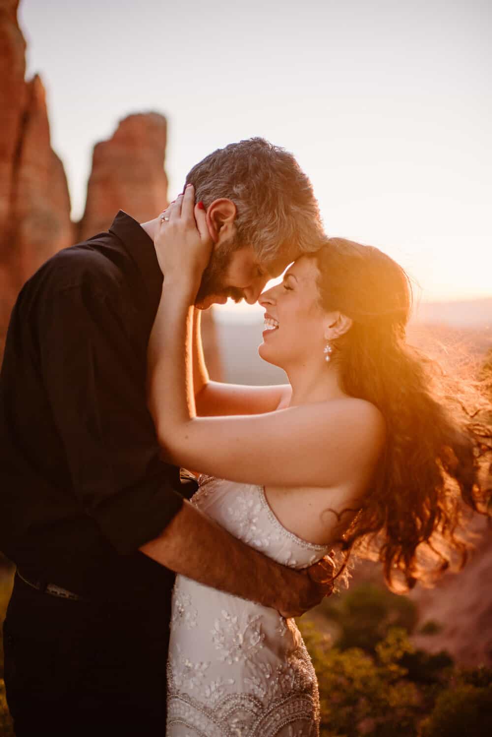 A bride and groom embrace as the wind swepts her hair on the top of Cathedral Rock. 
