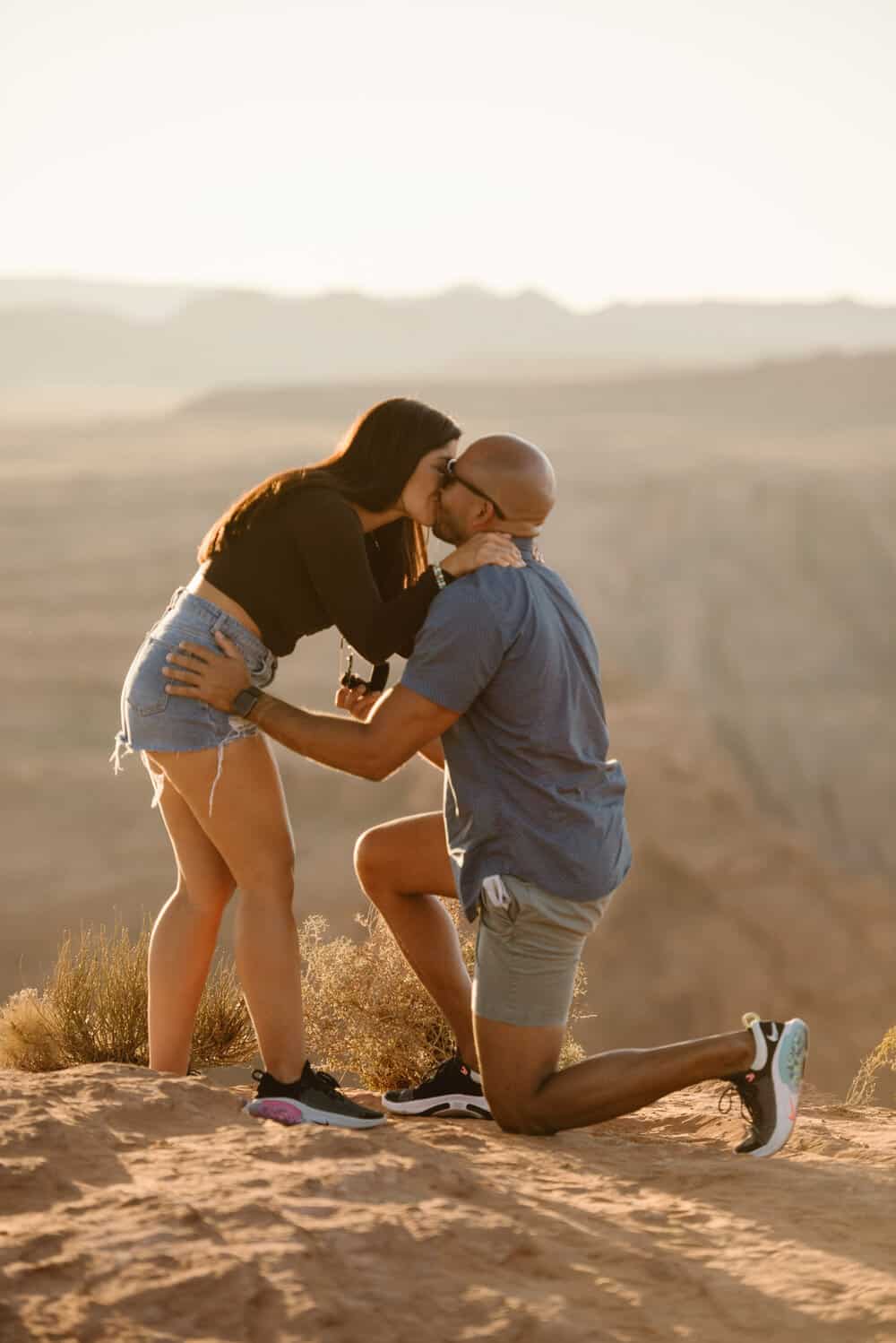 A woman kisses her partner as he proposes to her. 