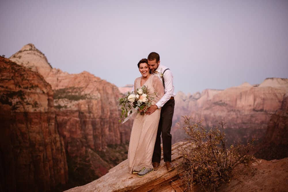 A bride laughs as her groom hugs her at sunset in Zion National Park.