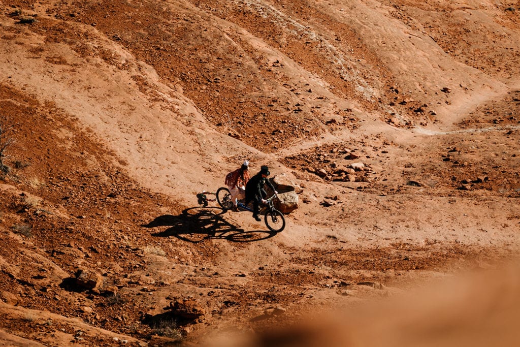 A couple rides a tantum mountain bike as they ride away from their ceremony.