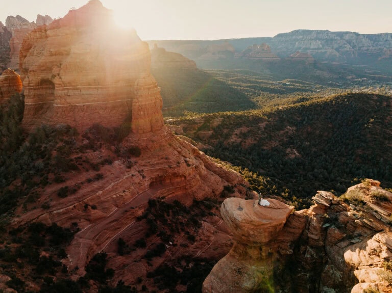 A couple stand together with the sun rising in the background