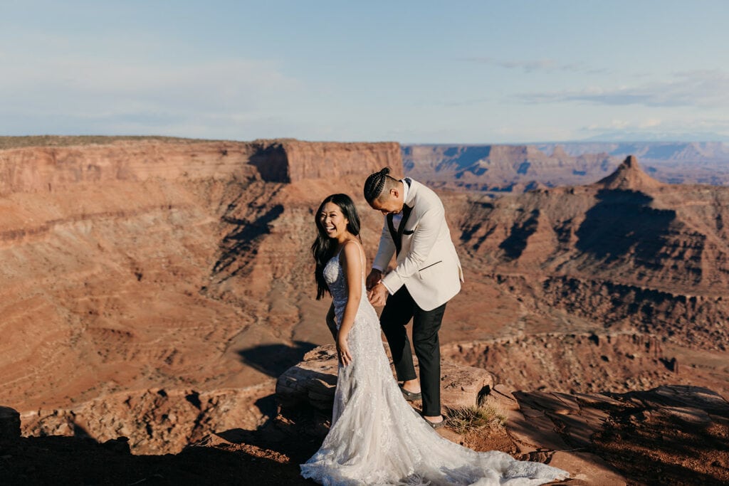 The groom helps the bride get into her dress. 