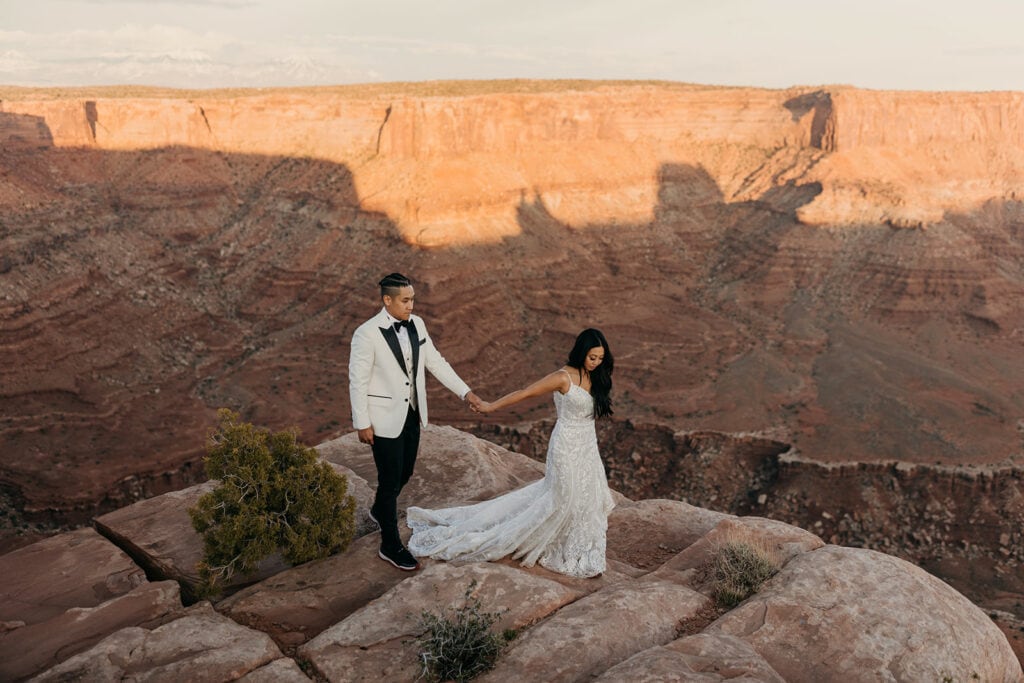 The bride leads the groom along the cliff side.
