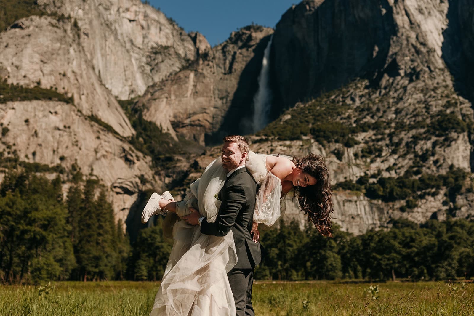 A groom carries his bride around Yosemite Meadows.
