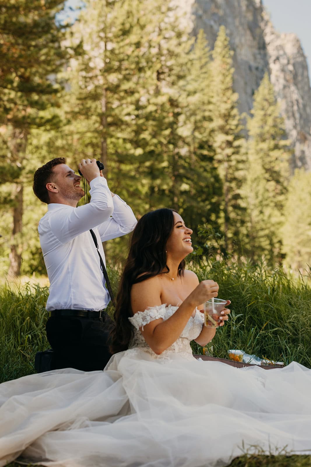 A couple sits in the El Cap Meadow having a picnic as they watch climbers.