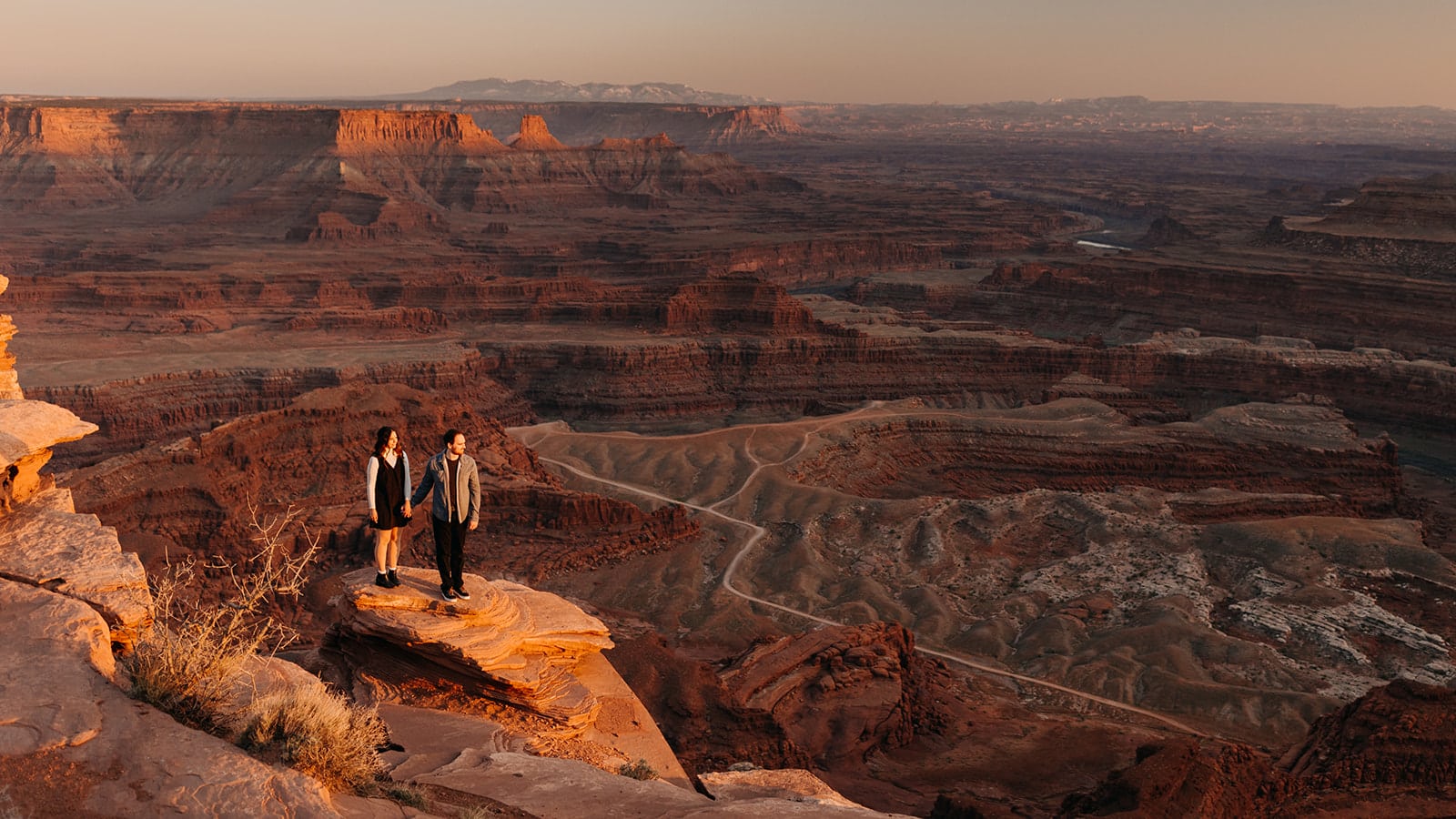A man and woman look out at the view below at a high up vista point in Moab Utah