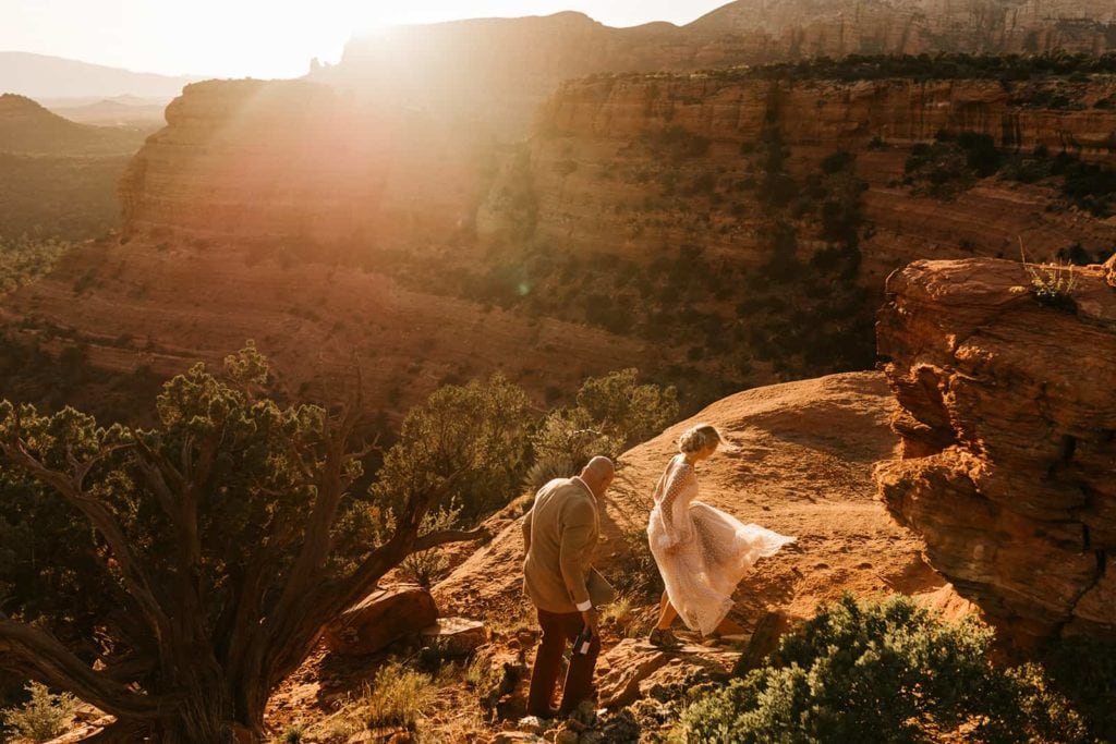 A bride and groom walk together to a vista ledge in Sedona Arizona.