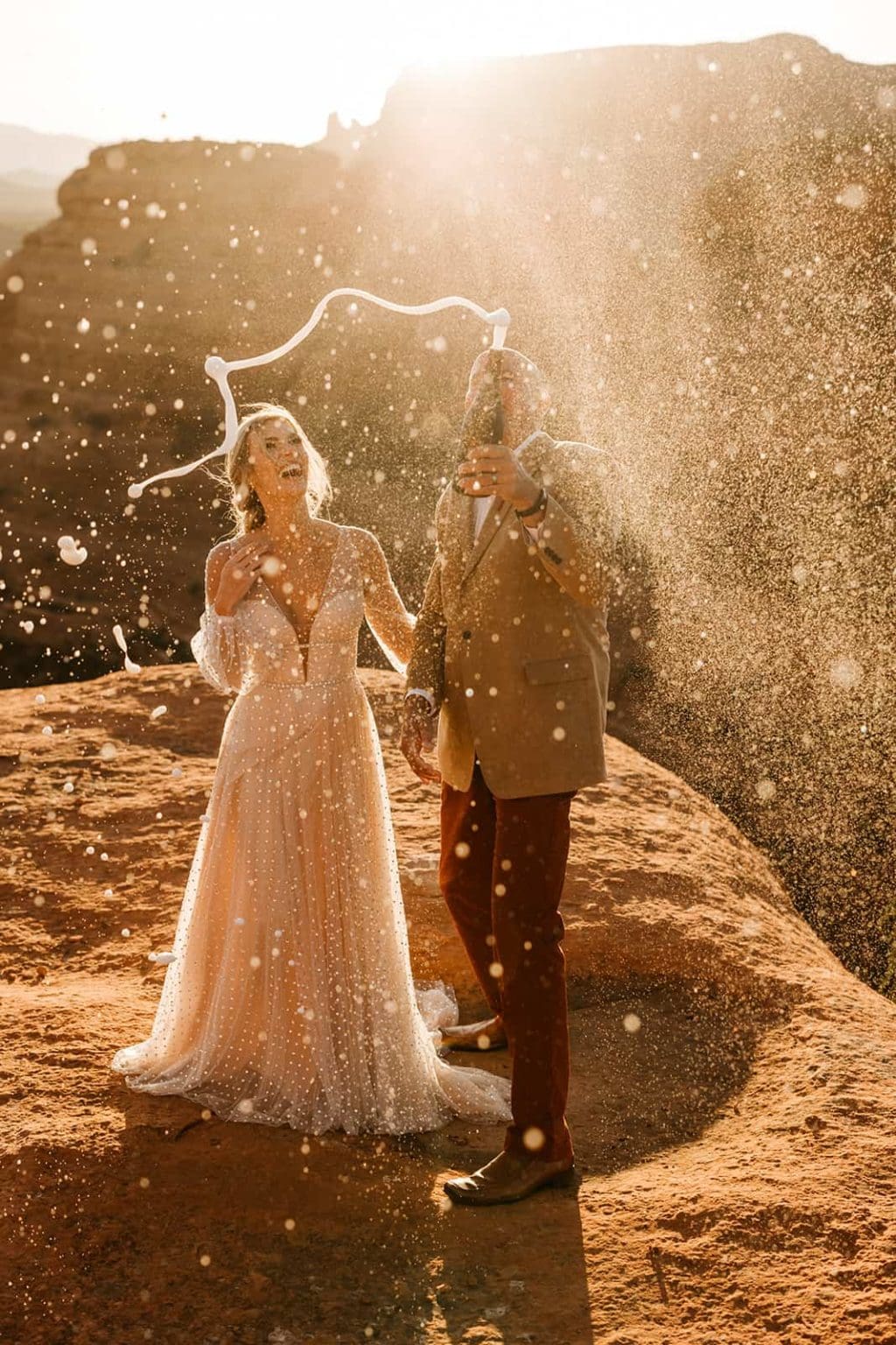 A groom sprays a bottle of champagne while the bride smiles in Sedona.