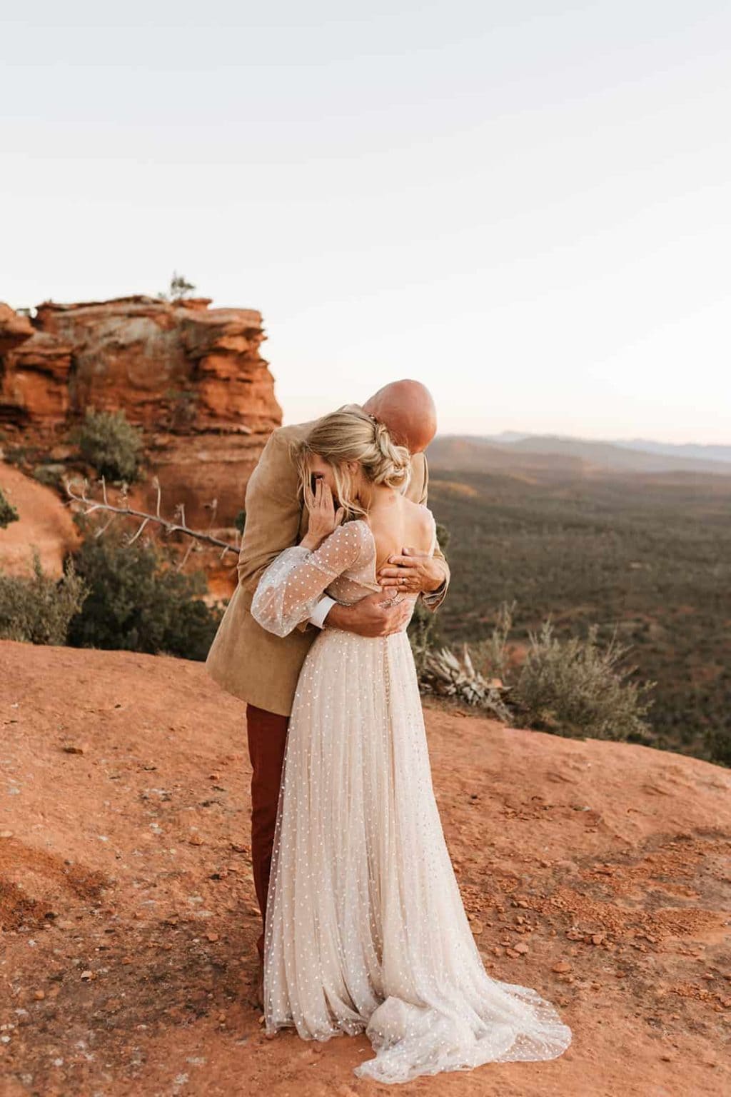 A bride wipes her tear away as her and her groom embrace each other in Sedona.