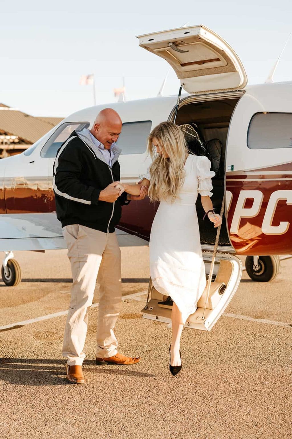 A man helps his partner to exit his airplane.