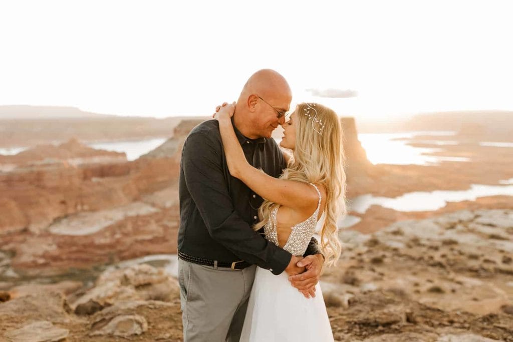 A couple embraces each other as the sun rises behind them.