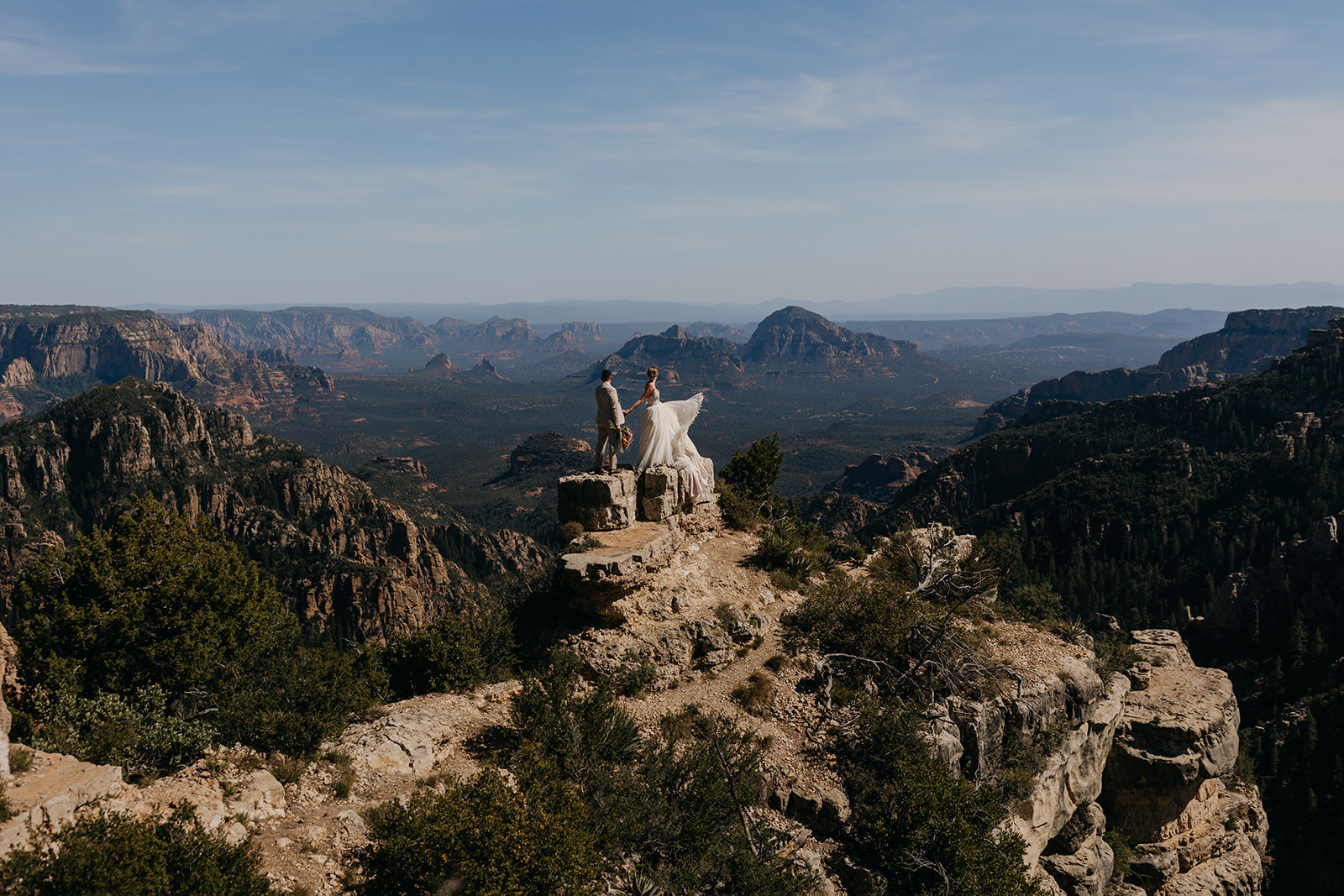 A bride plays with her dress in the sunshine while standing on a vista.