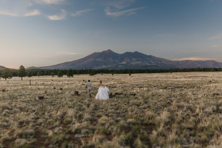 A couple runs in a field looking towards Humphrey's Peak.