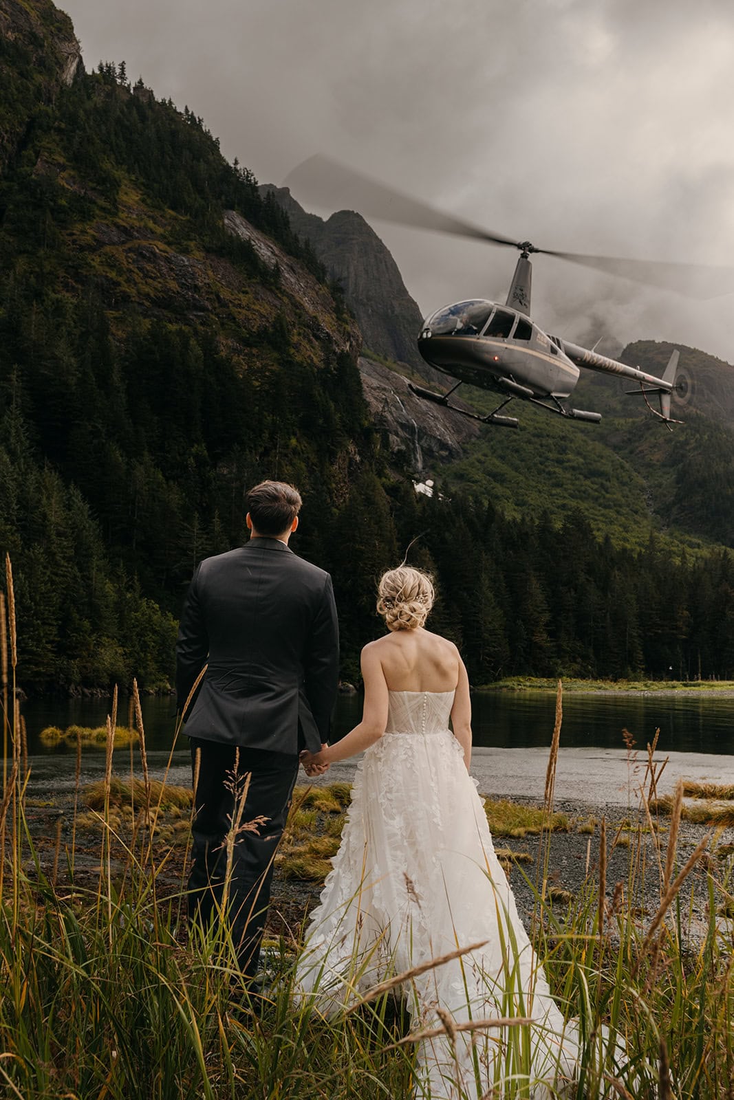 A couple holds hands and watches as a helicopter flies away.