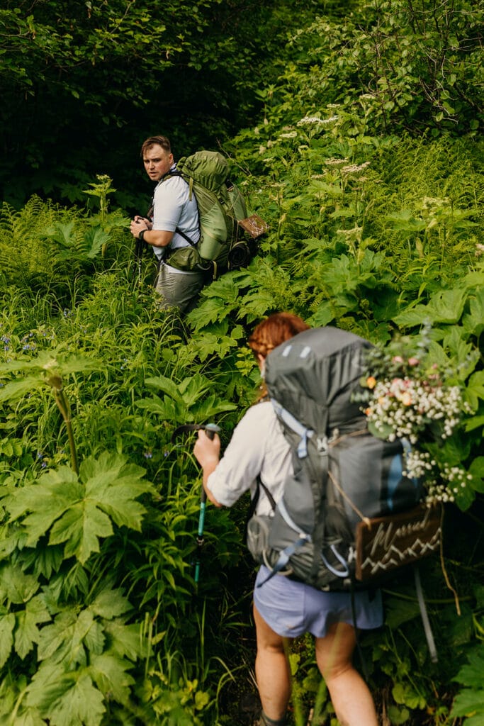 The groom looks back towards the bride on the trail.
