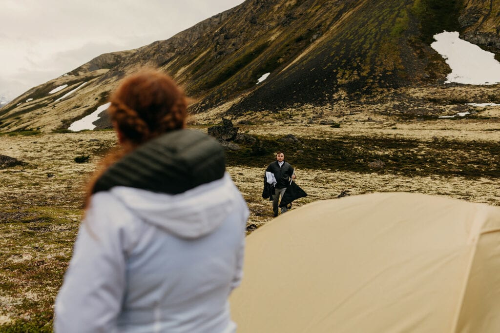 The bride watches as the groom walks towards the tent.