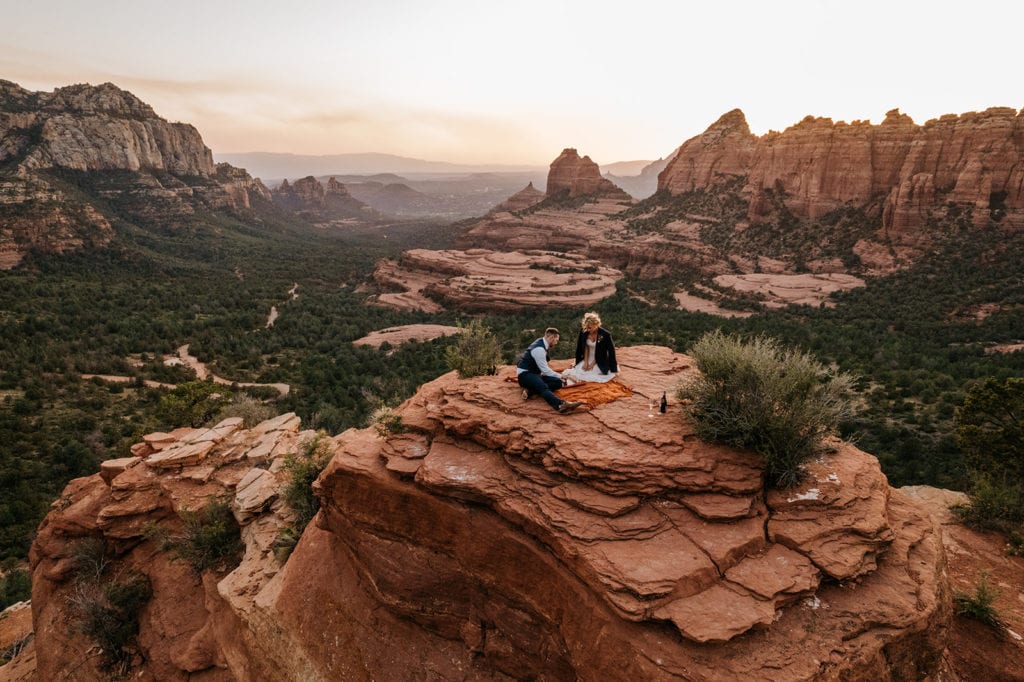 A couple plays a game of chess on top of a red rock overlook. 