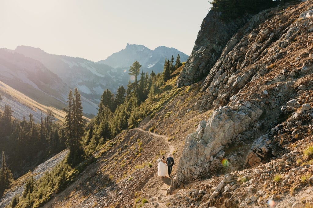 A wedding couple walks together down the trial in the sunlight.